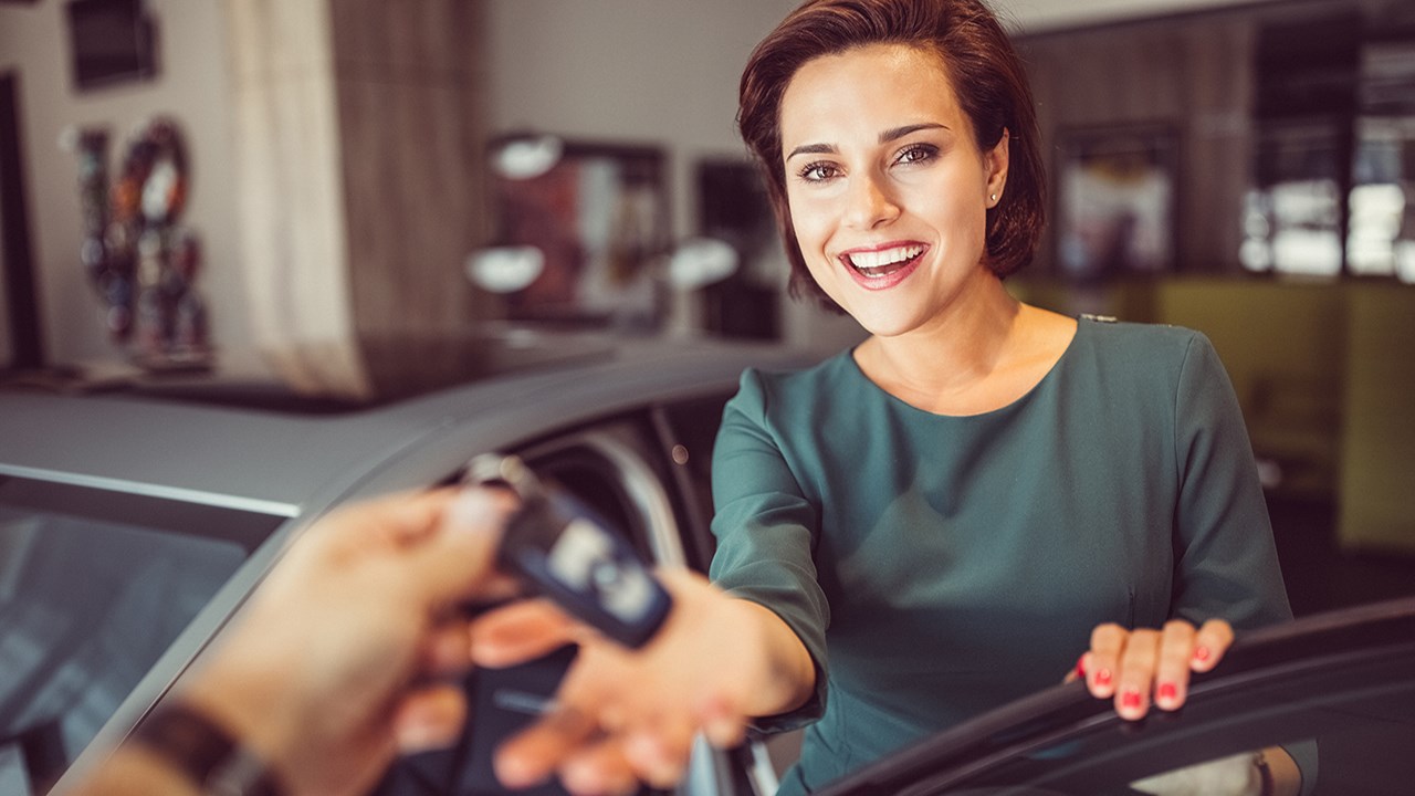 Women smiling receiving keys to her new car 